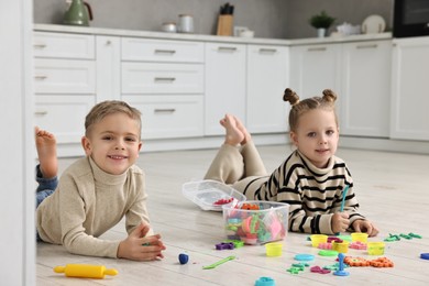 Photo of Cute little children playing together on warm floor in kitchen. Heating system