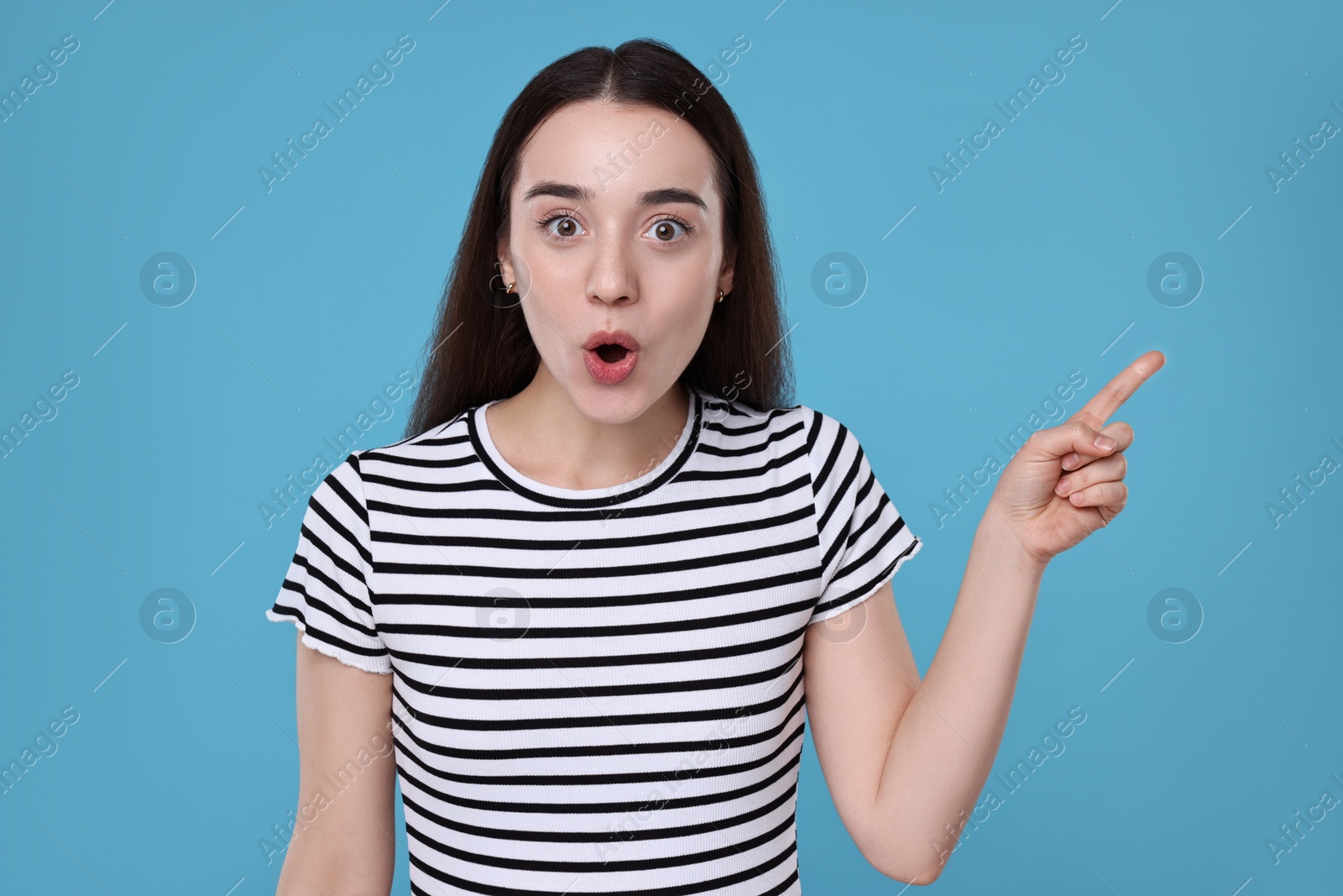 Photo of Portrait of surprised woman pointing at something on light blue background