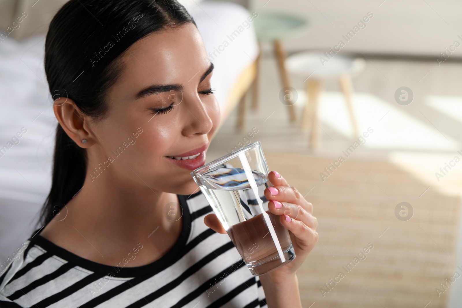 Photo of Young woman drinking water indoors, space for text. Refreshing drink