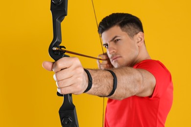 Photo of Man with bow and arrow practicing archery against yellow background, focus on hand
