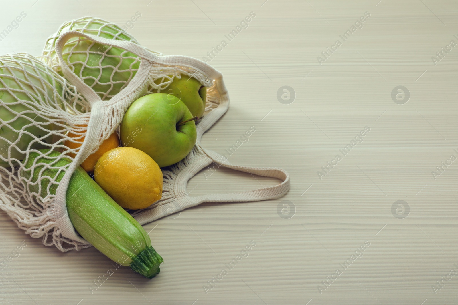 Photo of Net bag with vegetables and fruits on wooden table. Space for text