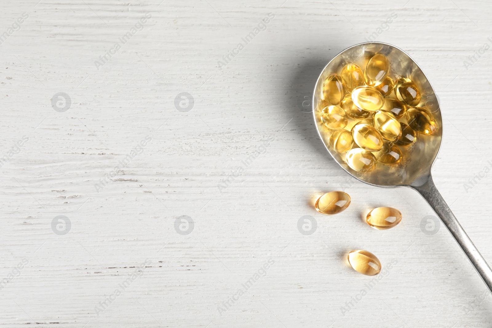 Photo of Spoon with cod liver oil pills and space for text on wooden background, flat lay