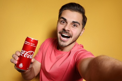 Photo of MYKOLAIV, UKRAINE - NOVEMBER 28, 2018: Young man taking selfie with Coca-Cola can on color background