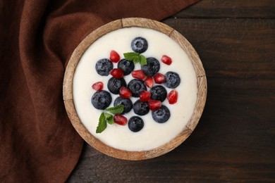 Photo of Bowl of delicious semolina pudding with blueberries, pomegranate and mint on wooden table, top view