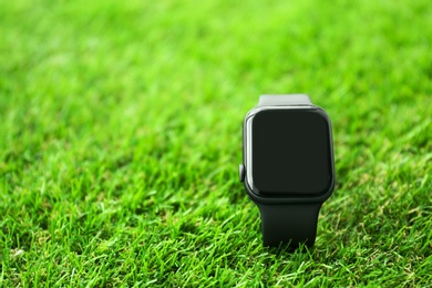 Photo of Stylish smart watch on green grass, closeup. Space for text