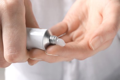 Photo of Woman squeezing out ointment from tube on her finger, closeup