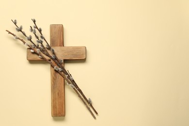 Photo of Wooden cross and willow branches on beige background, top view with space for text. Easter attributes