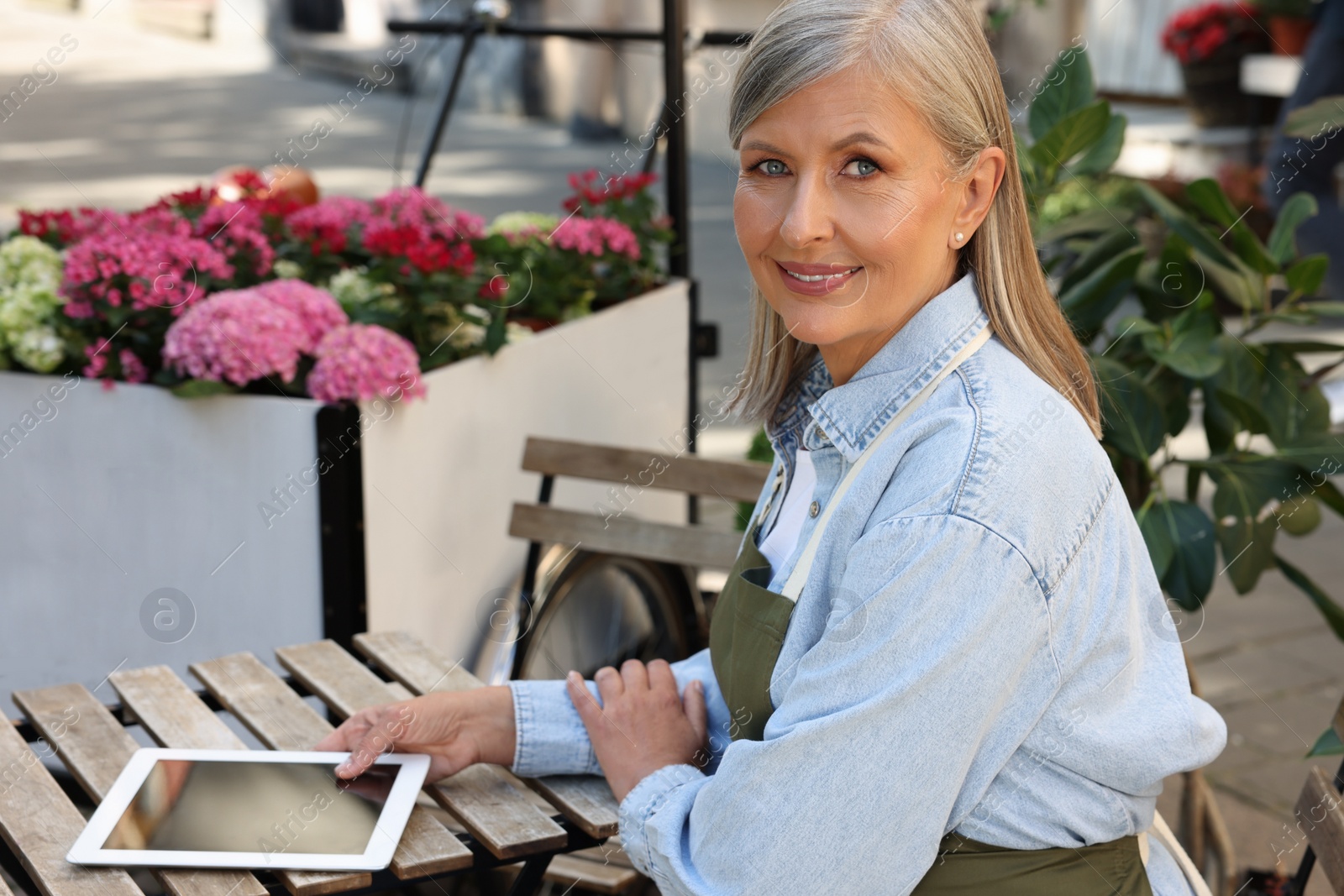 Photo of Happy business owner with tablet at table near her flower shop outdoors