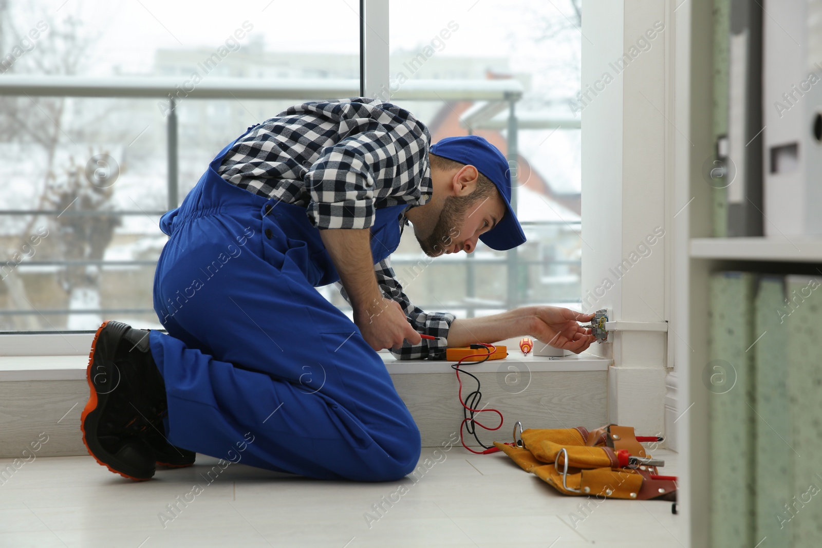 Photo of Electrician with screwdriver repairing power socket indoors