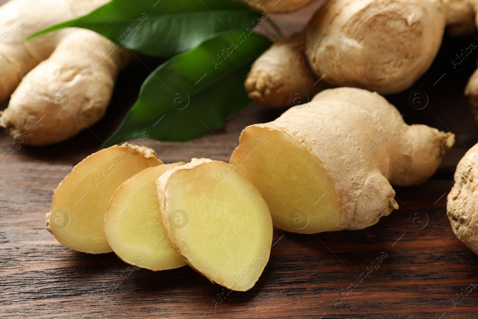 Photo of Cut and whole fresh ginger with leaves on wooden table, closeup