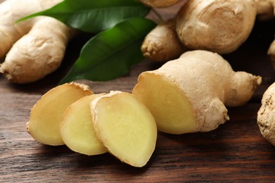 Cut and whole fresh ginger with leaves on wooden table, closeup