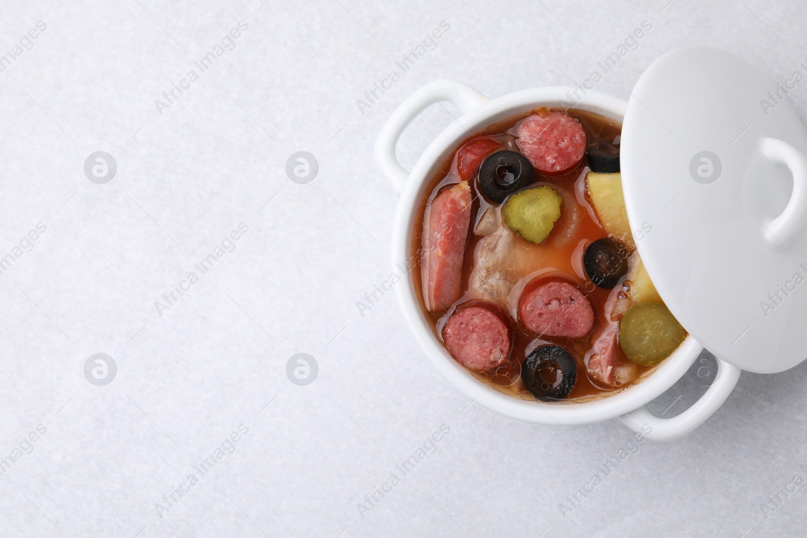 Photo of Meat solyanka soup with thin dry smoked sausages in pot on light table, top view. Space for text