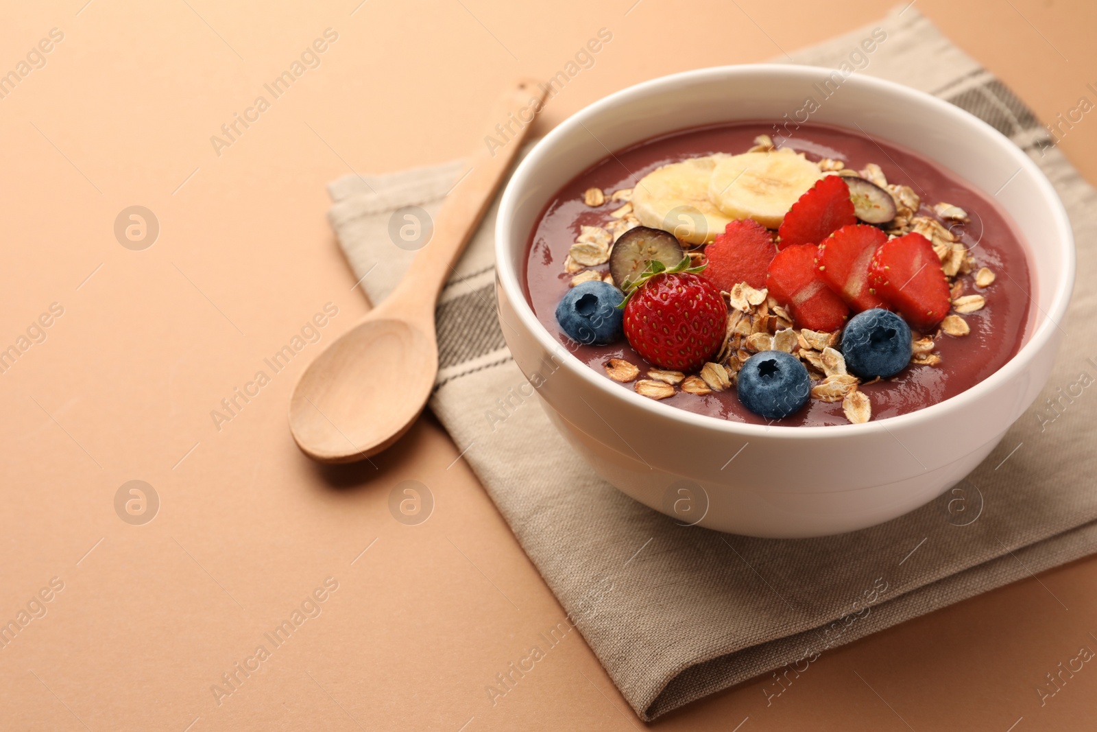 Photo of Delicious smoothie bowl with fresh berries, banana and granola on pale orange background. Space for text