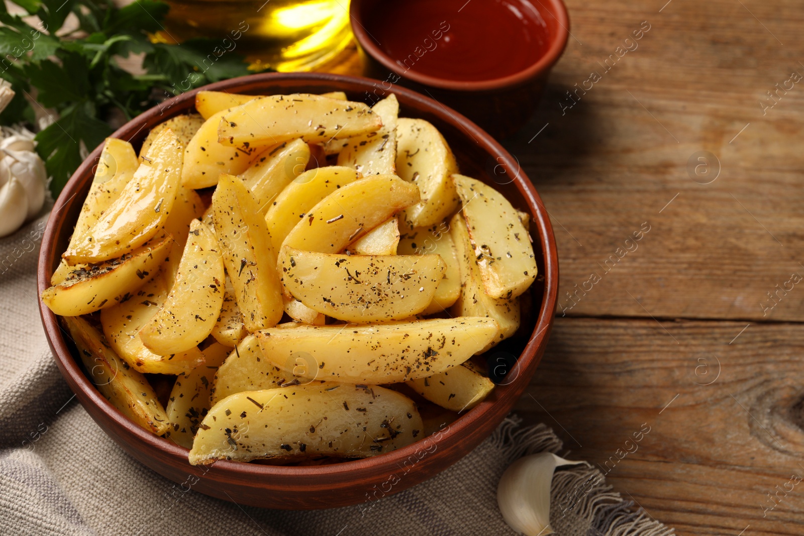 Photo of Bowl with tasty baked potato wedges, sauce and spices on wooden table