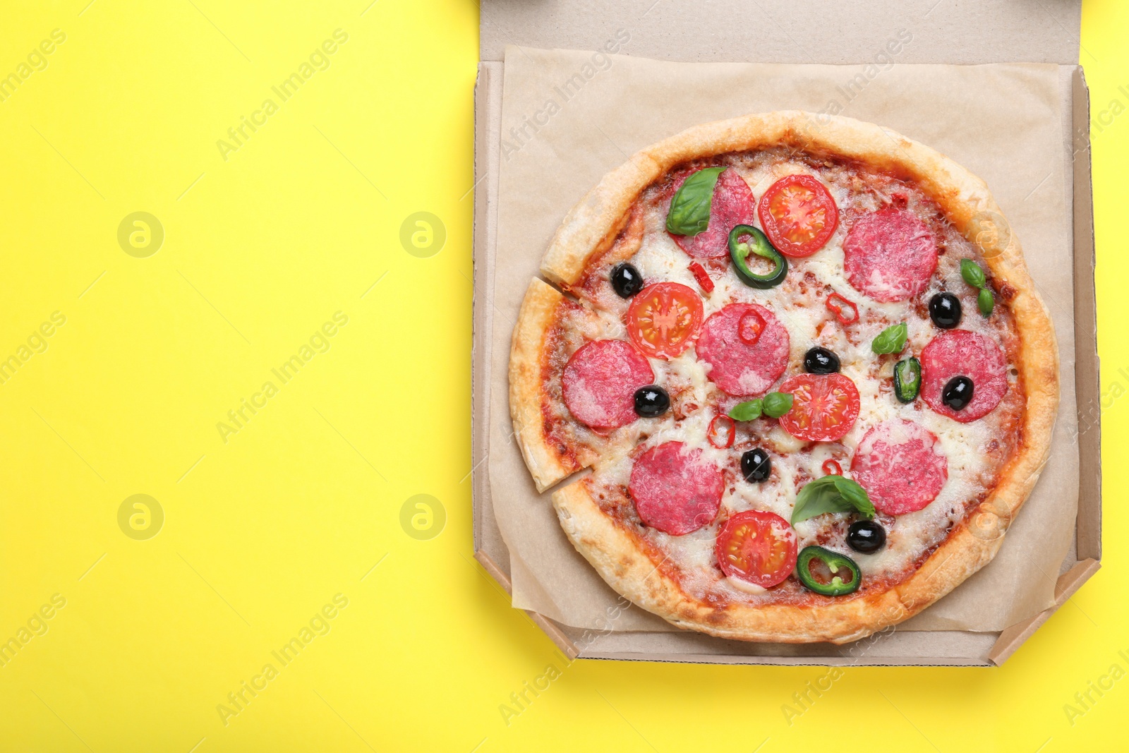Photo of Delicious pizza Diablo in cardboard box on yellow background, top view. Space for text