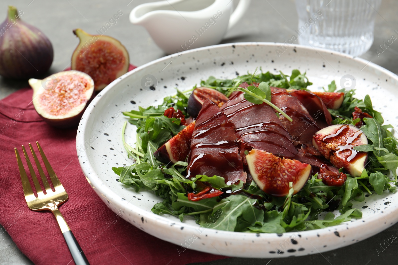 Photo of Plate of tasty bresaola salad with figs, sun-dried tomatoes, balsamic vinegar and fork on table, closeup