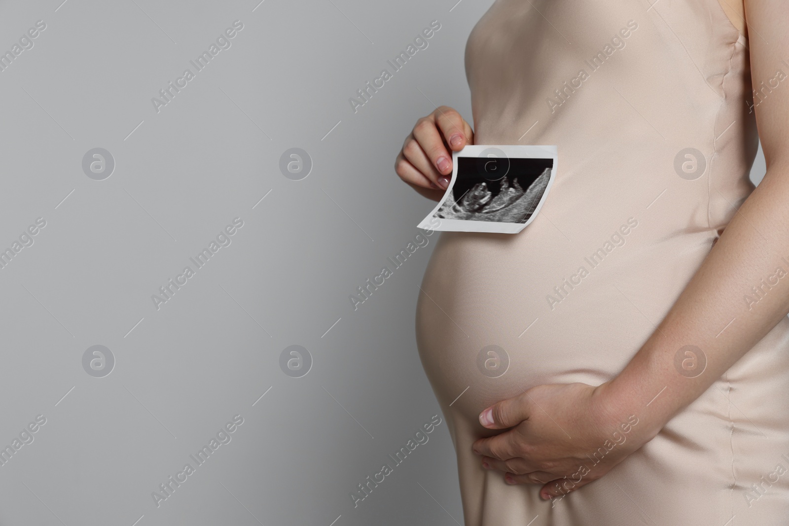 Photo of Pregnant woman with ultrasound picture of baby on light grey background, closeup. Space for text