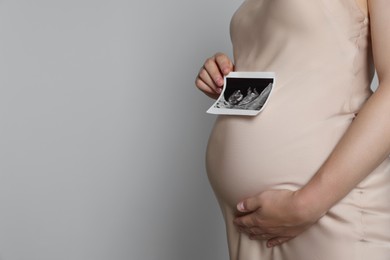 Pregnant woman with ultrasound picture of baby on light grey background, closeup. Space for text