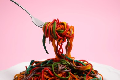 Photo of Taking delicious spaghetti painted with different food colorings on pink background, closeup