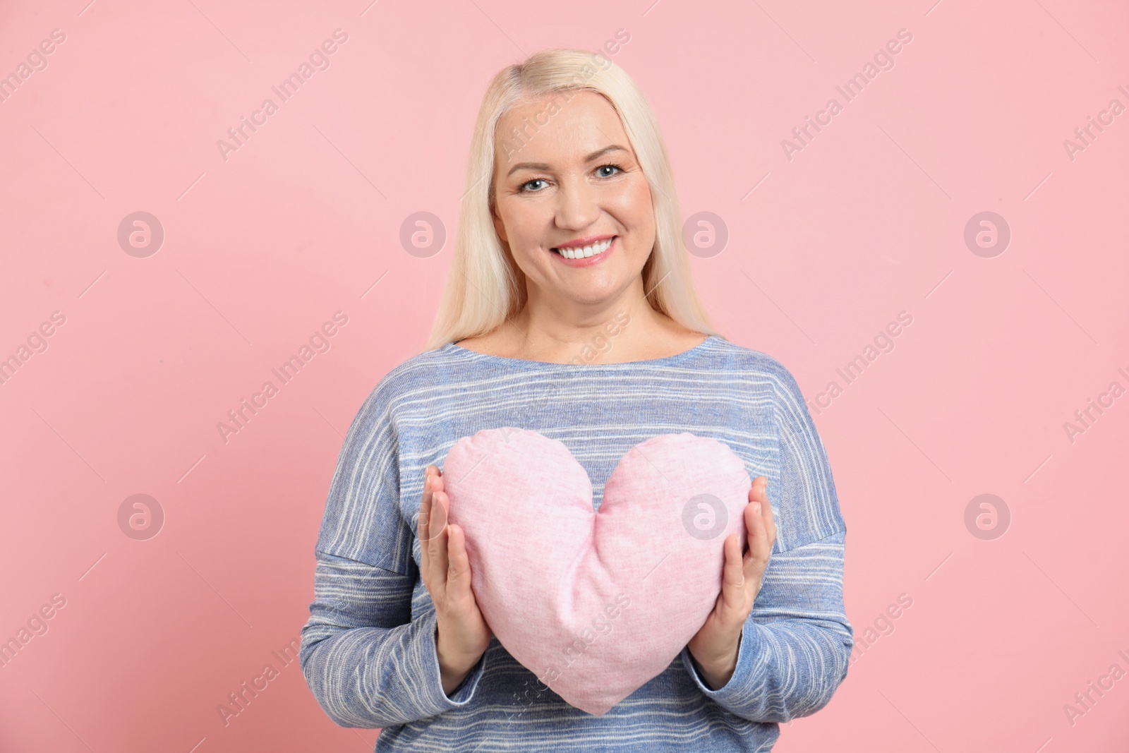 Photo of Portrait of mature woman with decorative heart shaped pillow on color background