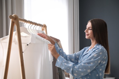 Photo of Woman taking shirt from rack with stylish clothes in room