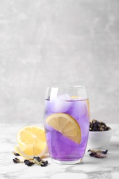 Photo of Glass of organic blue Anchan with lemon and ice on white marble table, space for text. Herbal tea
