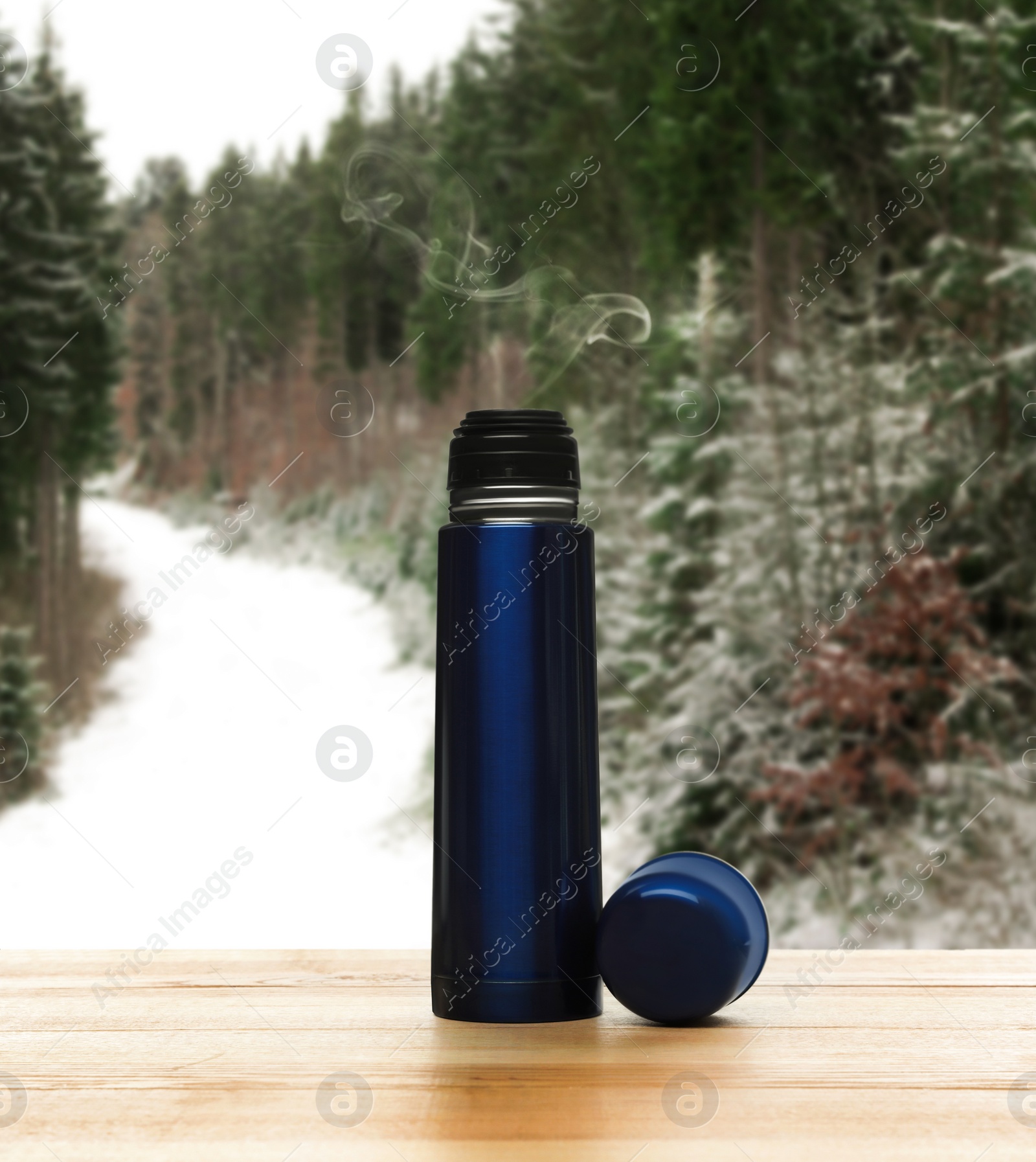 Image of Blue thermos on wooden table in snowy forest