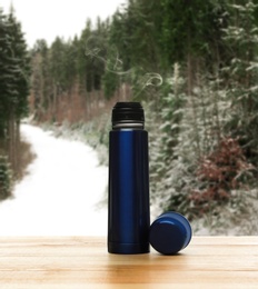 Blue thermos on wooden table in snowy forest