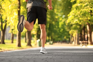 Photo of Sporty man jogging in park on sunny day, closeup. Space for text