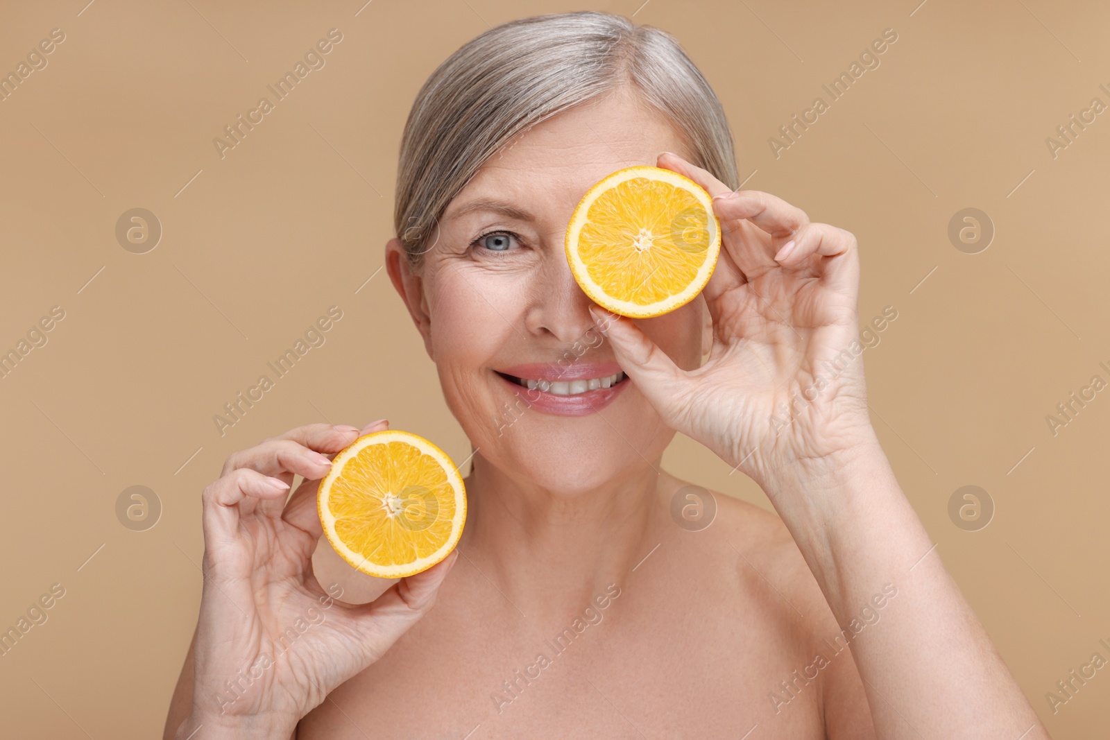 Photo of Beautiful woman with halves of orange rich in vitamin C on beige background