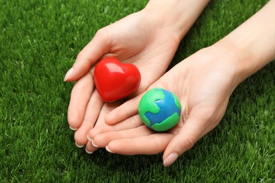 Photo of Happy Earth Day. Woman with plasticine planet and decorative heart on green grass, closeup