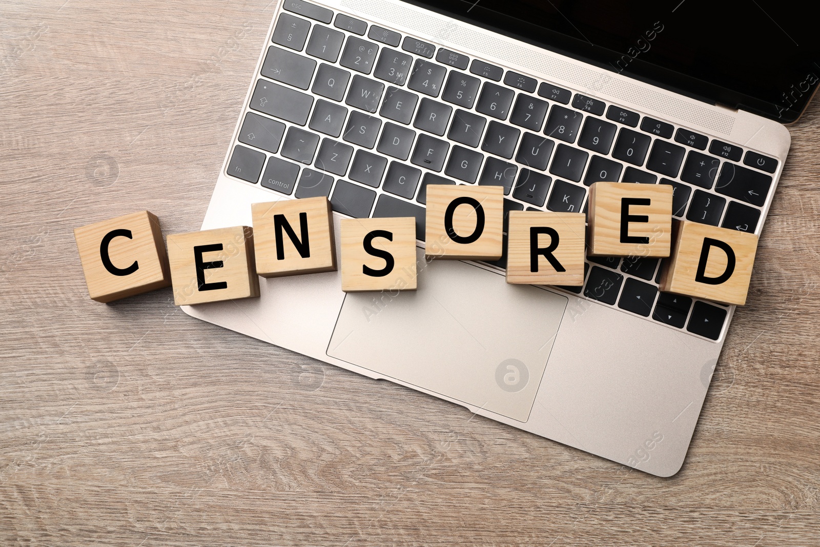 Photo of Cubes with word Censored and laptop on wooden table, flat lay