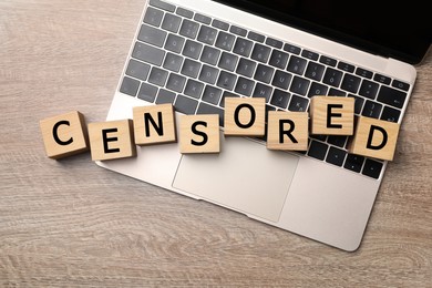 Cubes with word Censored and laptop on wooden table, flat lay