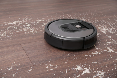 Removing groats from wooden floor with robotic vacuum cleaner at home. Space for text