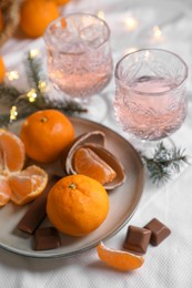 Delicious ripe tangerines, chocolates, festive lights and glasses of wine on white bedsheet