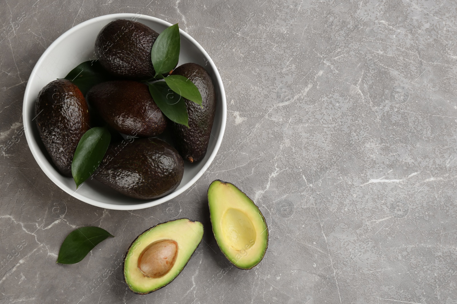 Photo of Whole and cut avocados on grey marble table, flat lay. Space for text