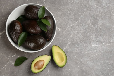 Whole and cut avocados on grey marble table, flat lay. Space for text