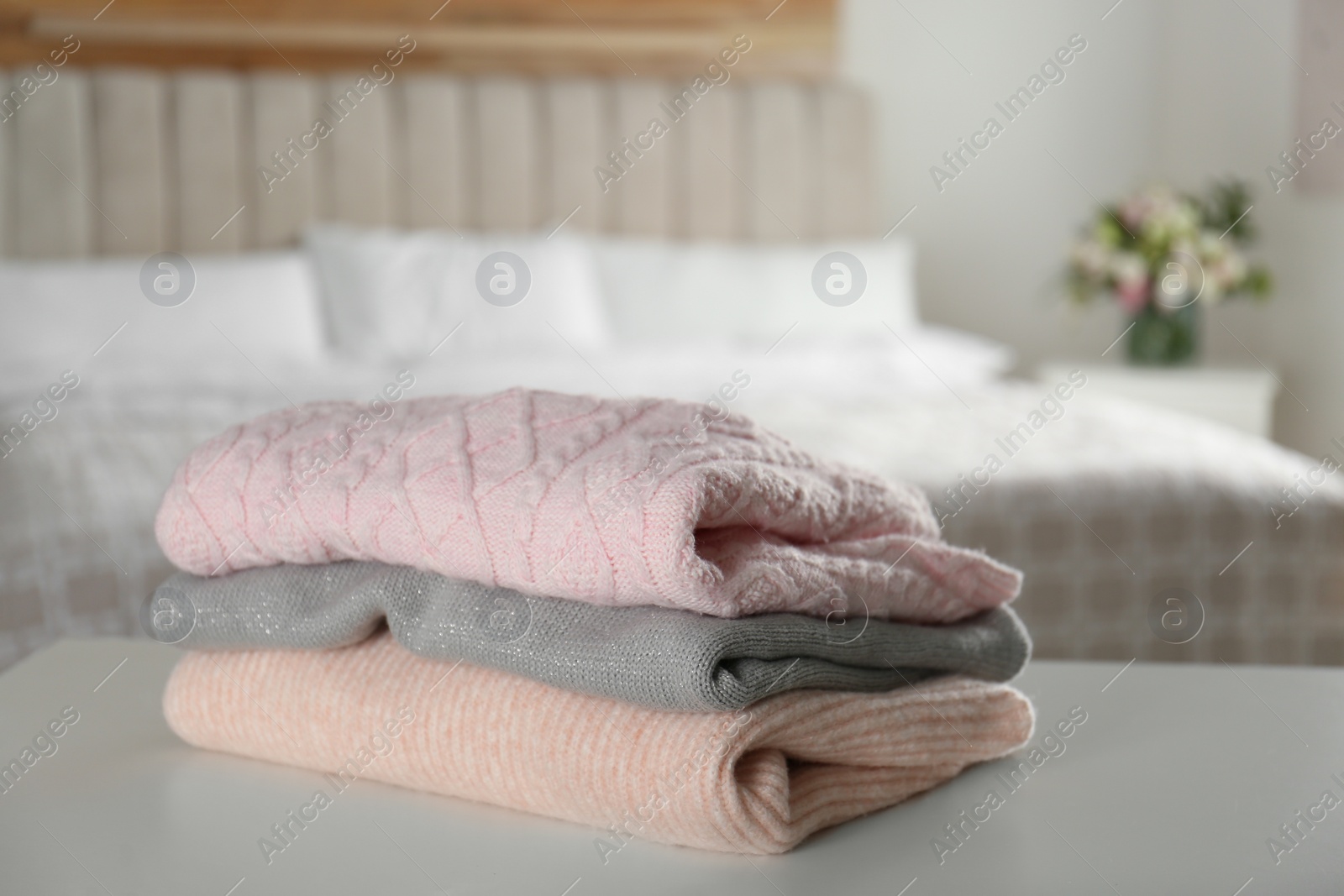 Photo of Stack of knitted sweaters on white table indoors