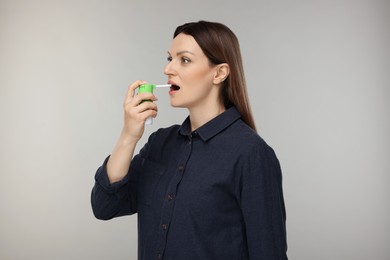 Woman using throat spray on grey background