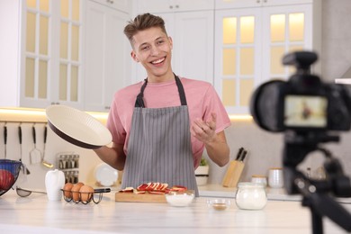 Photo of Smiling food blogger explaining something while recording video in kitchen