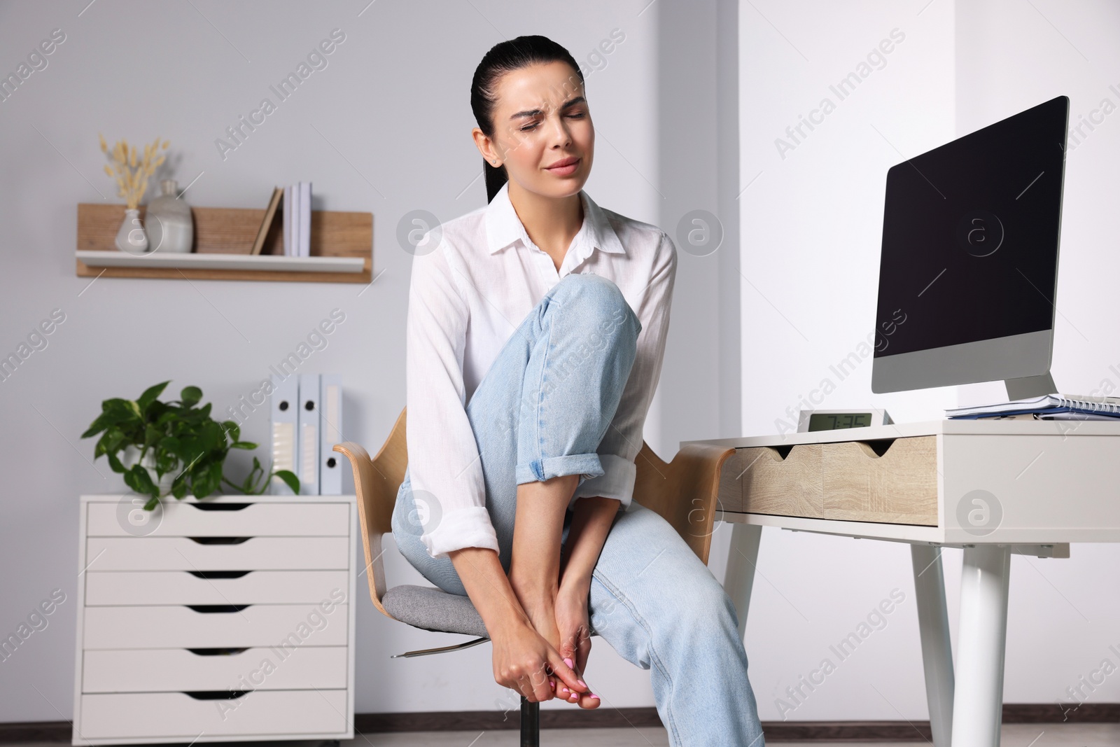 Photo of Young woman rubbing sore foot in office