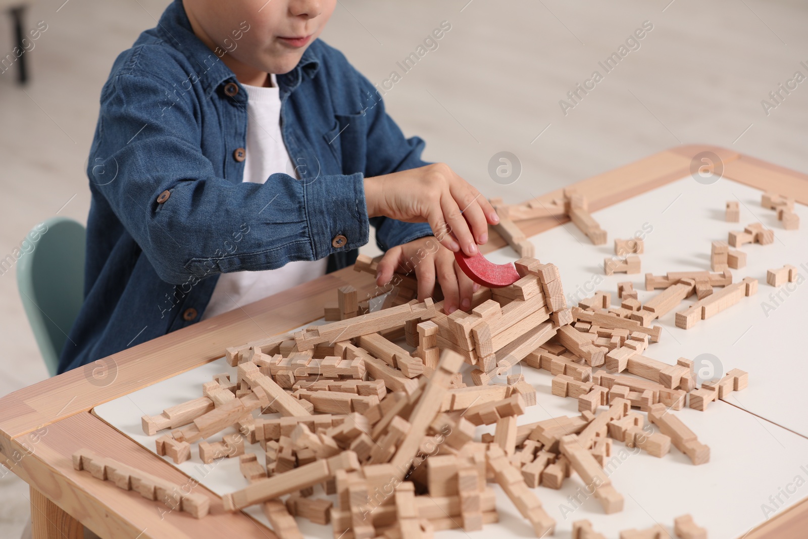 Photo of Little boy playing with wooden blocks at table indoors, closeup. Child's toy