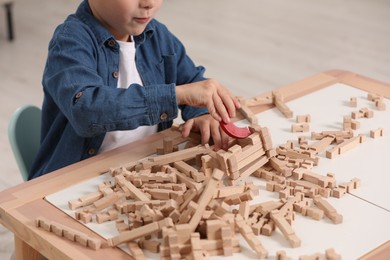 Photo of Little boy playing with wooden blocks at table indoors, closeup. Child's toy
