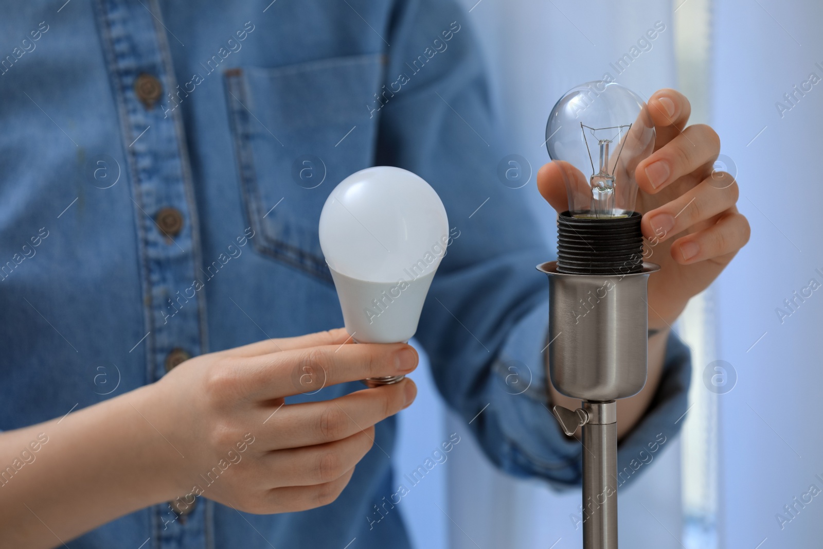 Photo of Woman changing incandescent light bulb for fluorescent one in lamp at home, closeup. Saving energy concept
