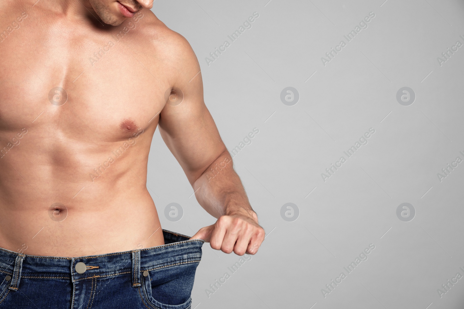 Photo of Young man with slim body in old big size jeans on grey background, closeup view. Space for text