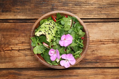 Photo of Fresh spring salad with flowers on wooden table, top view