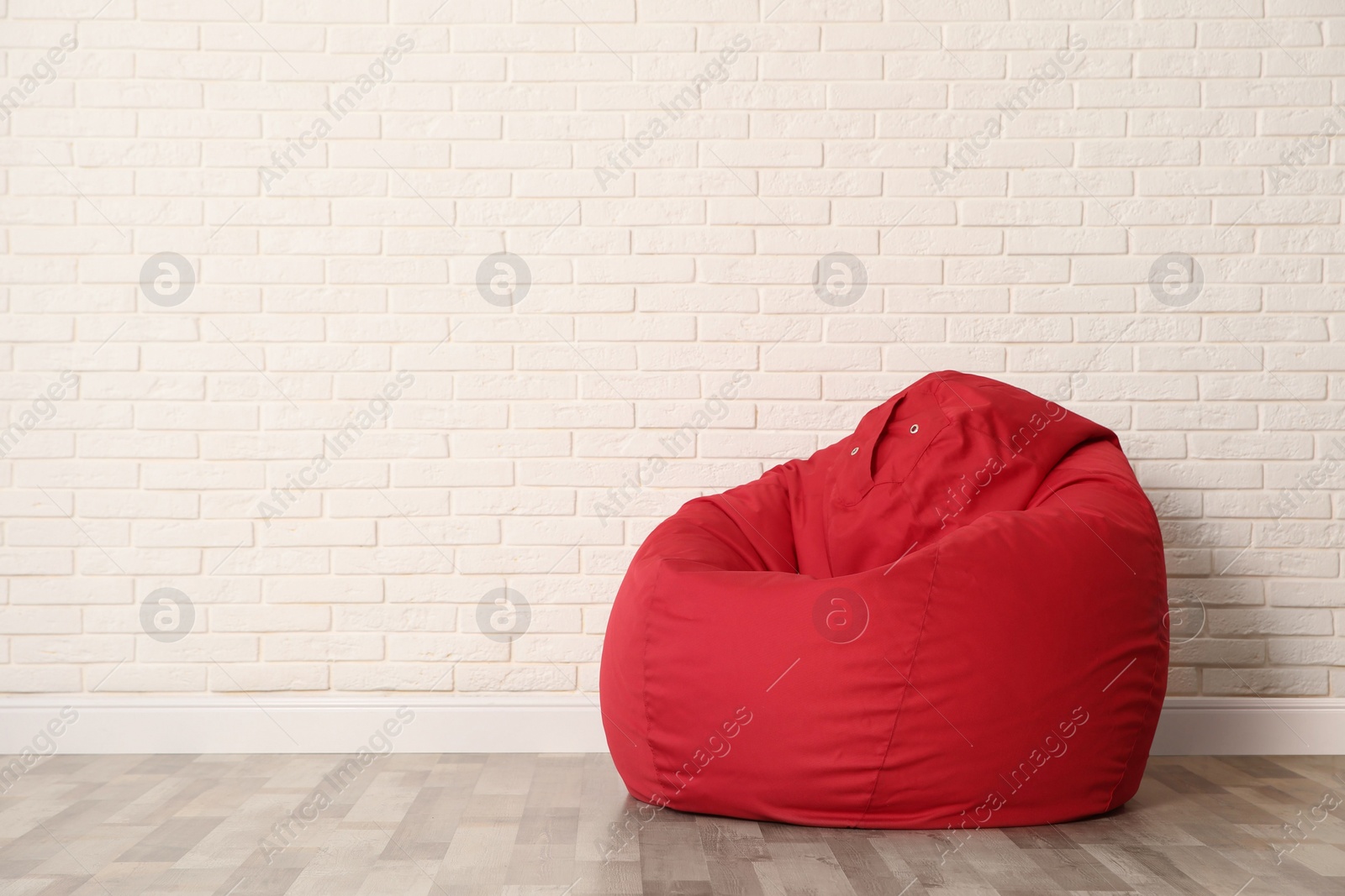 Photo of Red bean bag chair near white brick wall in room. Space for text