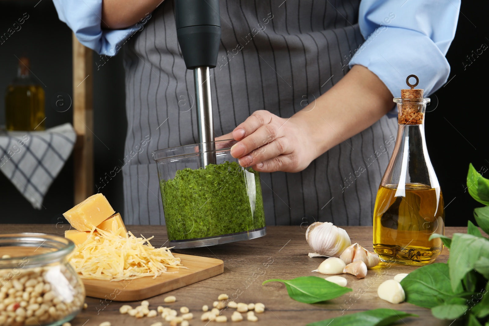 Photo of Woman blending pesto sauce in bowl at table, closeup