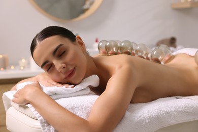 Photo of Cupping therapy. Woman with glass cups on massage couch in spa salon