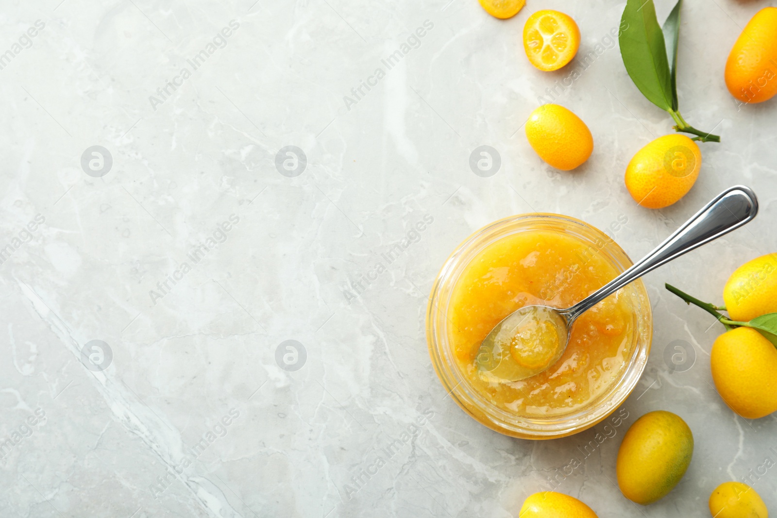 Photo of Delicious kumquat jam and fresh fruits on light grey marble table, flat lay. Space for text